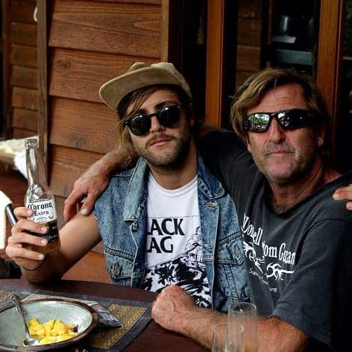 Two men wearing sunglasses are sitting at a table holding hands.